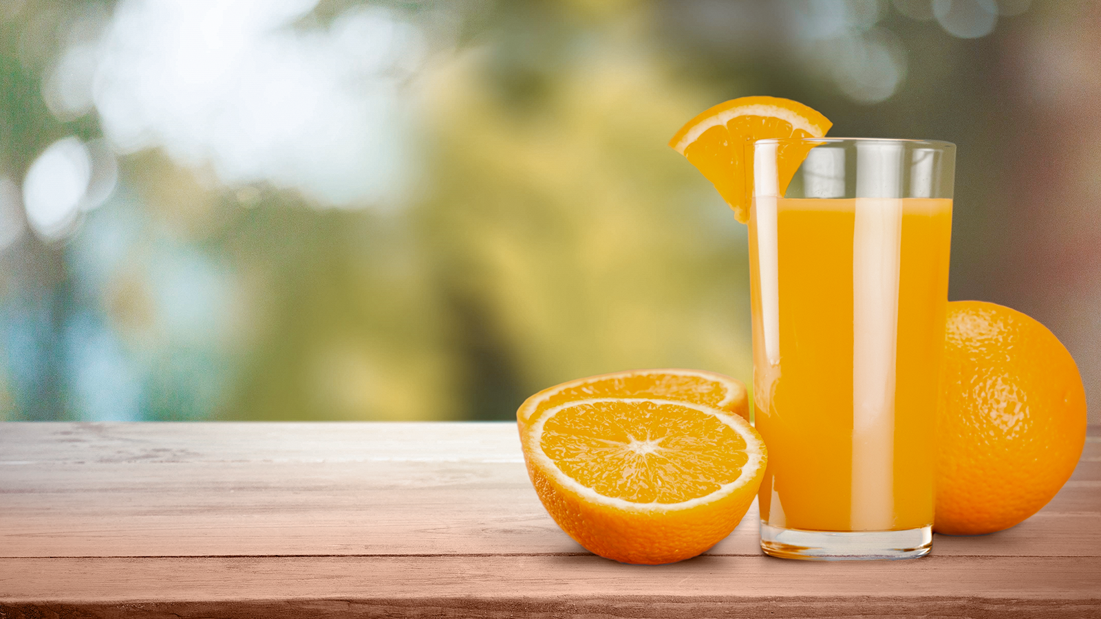 Ein Glas Orangensaft, neben dem zwei frische Orangen liegen