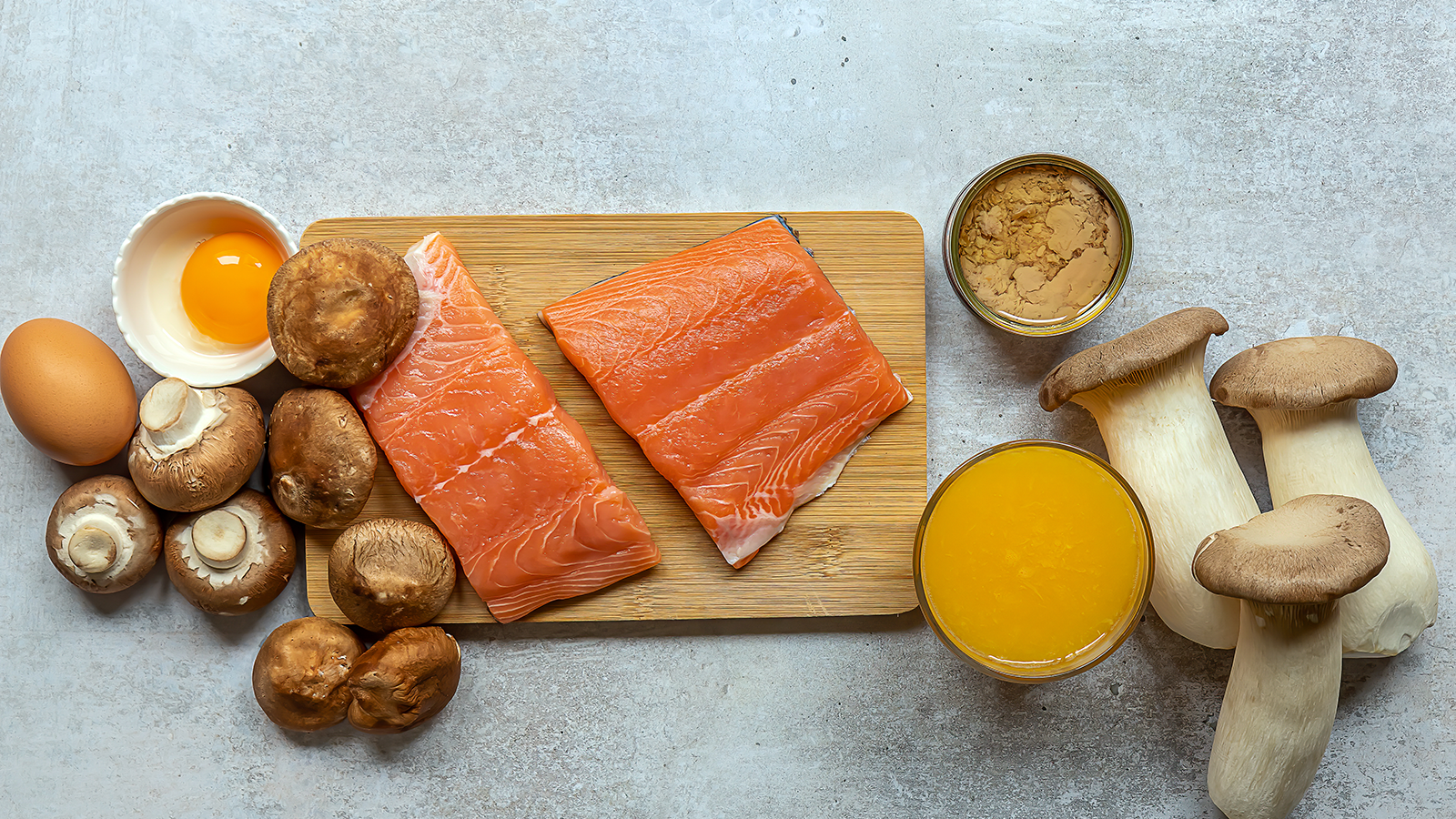 Ein Schneidebrett mit rohem Lachs, kleingeschnittenen Pilzen und daneben Eier