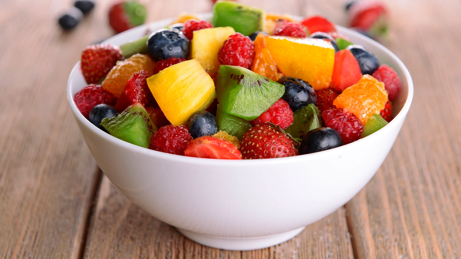 Weiße Obstschale auf einem Holztisch gefüllt mit Erdbeeren, Kiwis und Trauben