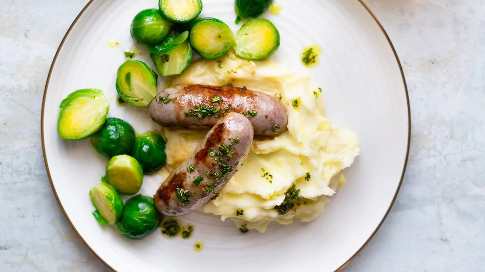 Rosenkohl in frischem Grün, auf einem Teller angerichtet mit Kartoffelstampf und Bratwurst