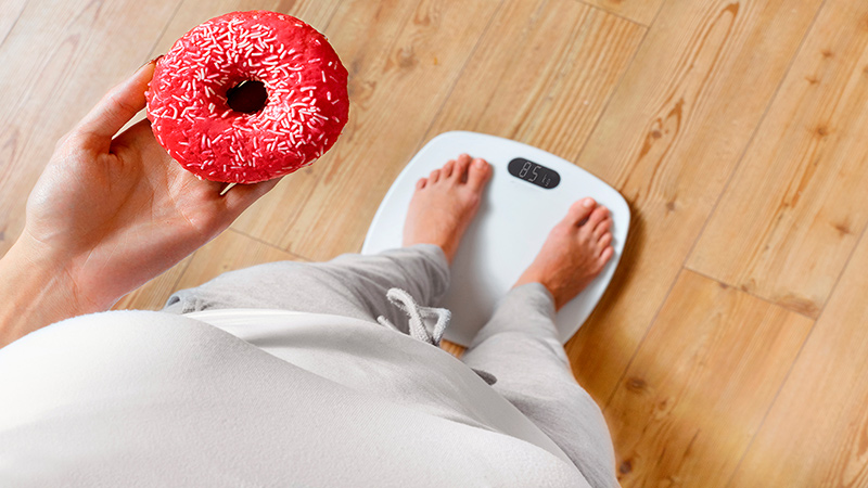 Eine Person steht auf einer Waage und hält einen Donut in den Hand