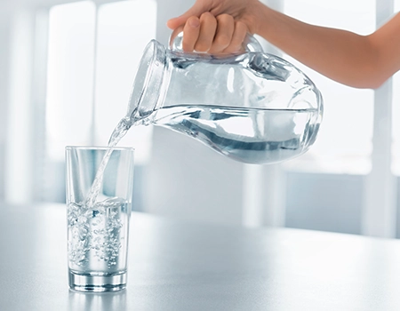 Frau gießt aus einer Karaffe Wasser in ein Glas