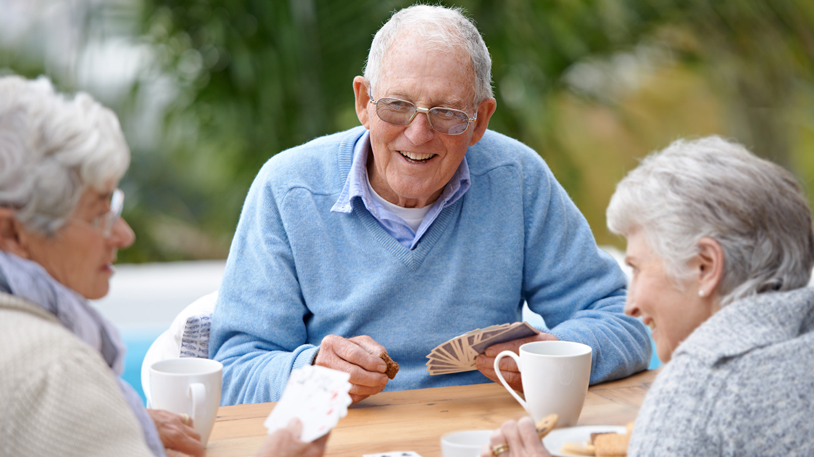 Drei Senioren sitzen zusammen und spielen freudig Karten