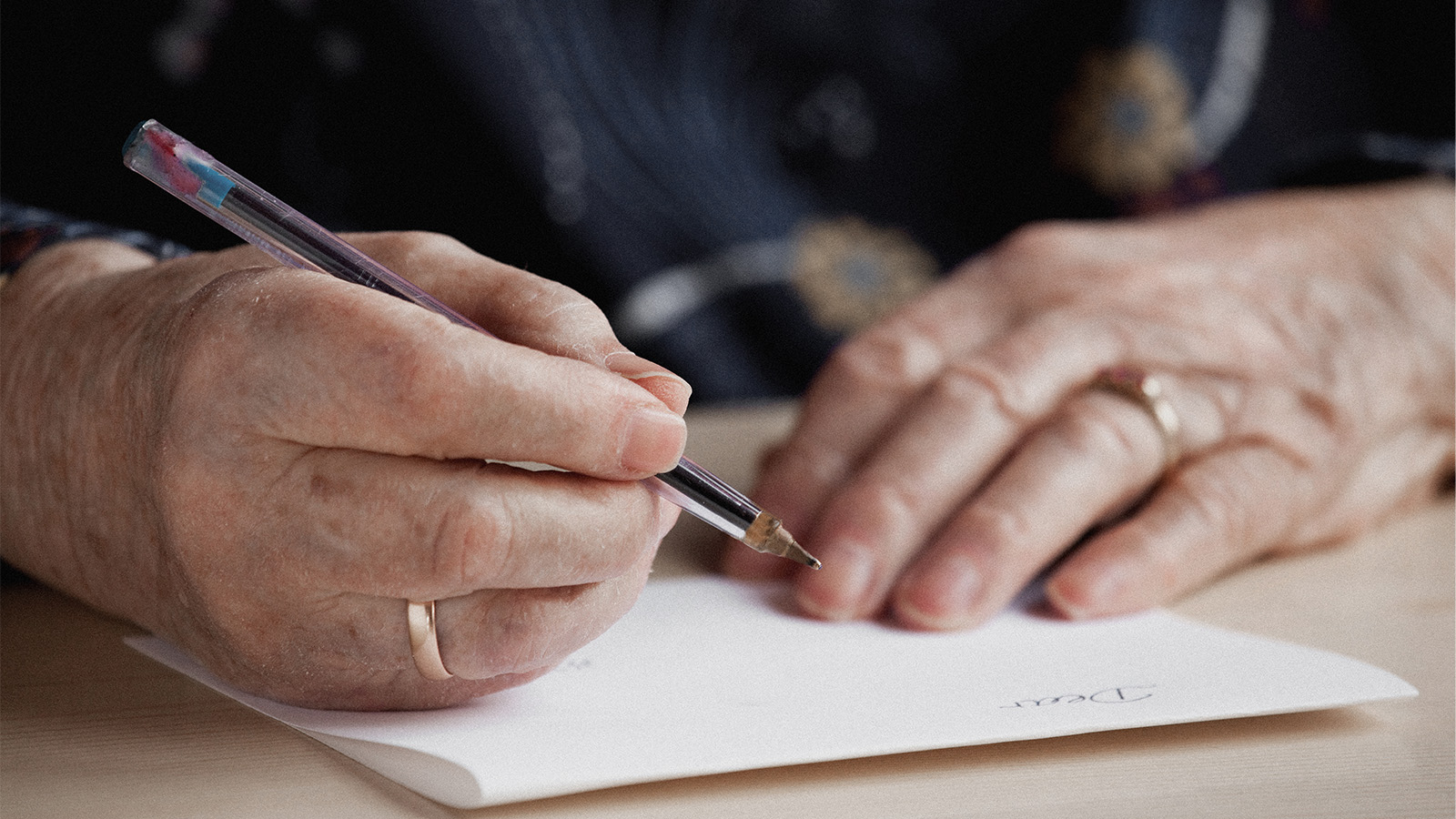 Ältere Frau, die mit einem Kuli etwas auf ein leeres Blatt Papier schriebt