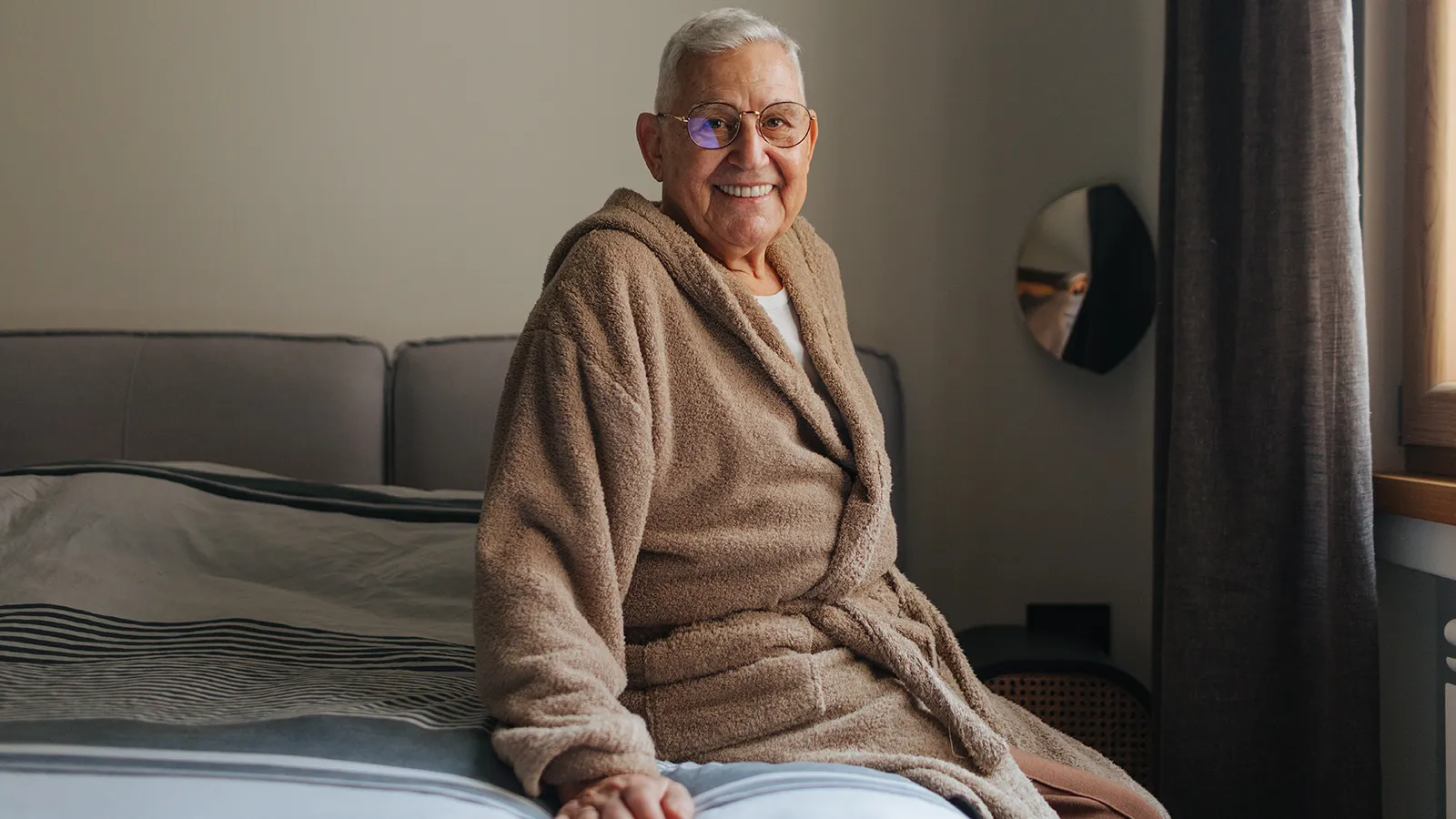 Älterer Mann sitzt im Bademantel auf seinem Bett