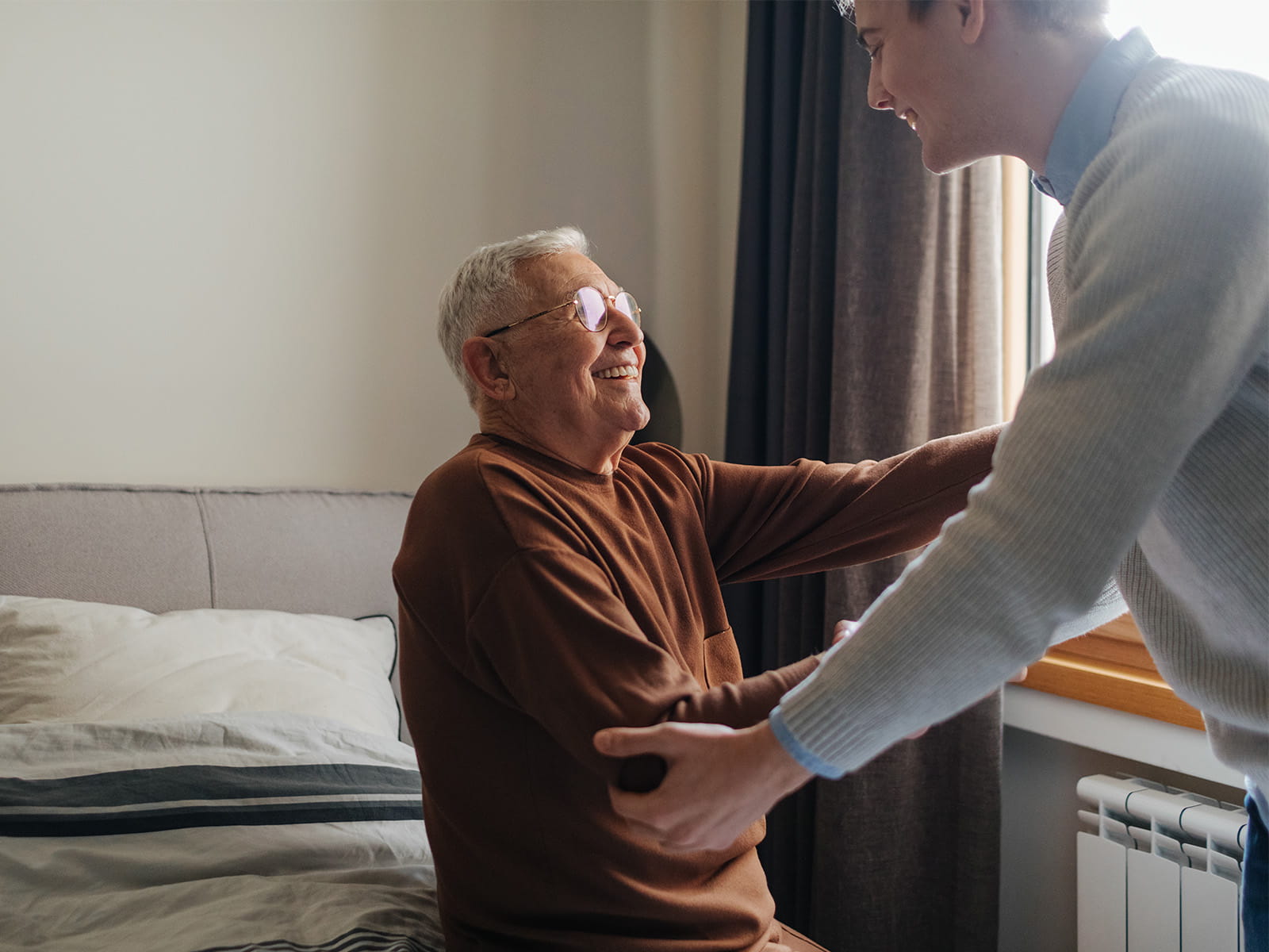 Der Enkel hilft seinem Opa beim Aufstehen aus dem Bett