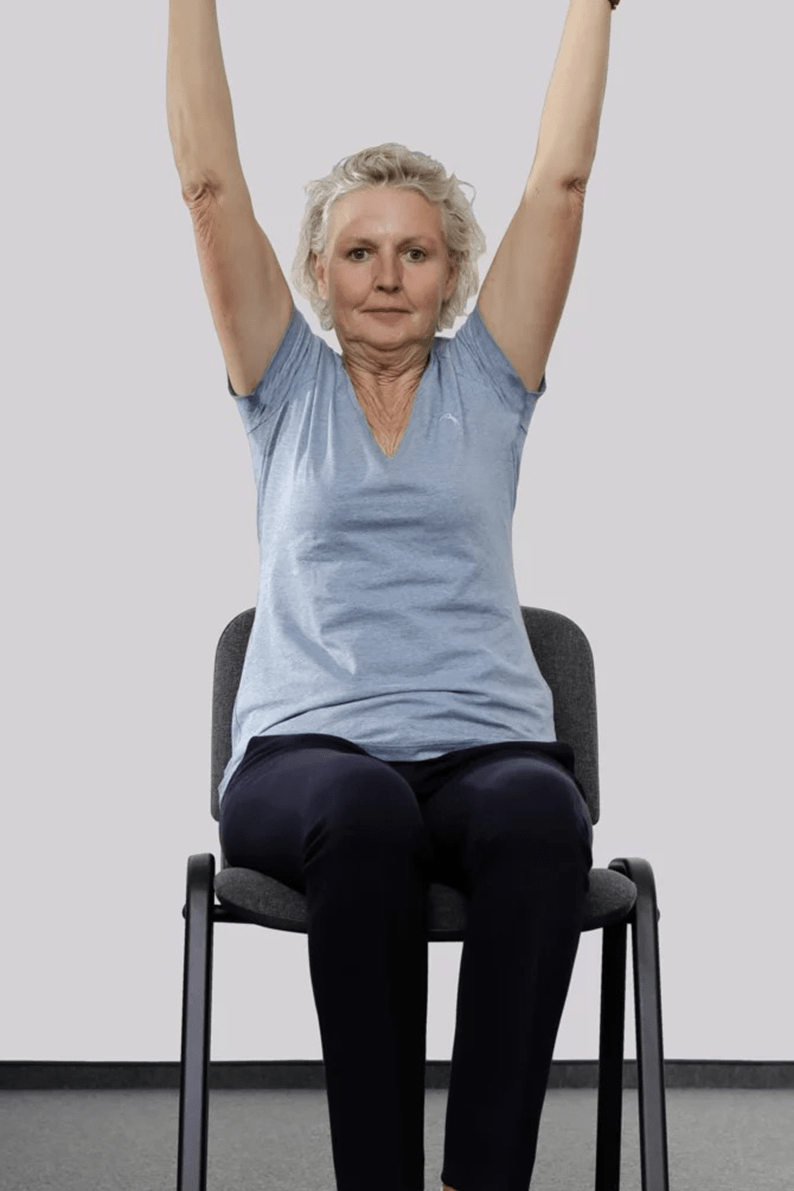 Frau sitzt auf einem Stuhl und reckt die Arme in die Höhe