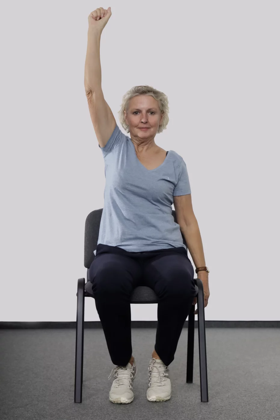 Frau sitzt auf einem Stuhl und streckt den rechten Arm in die Höhe