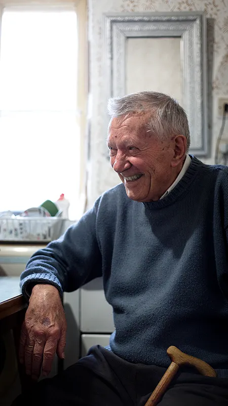 Ein älterer Mann sitzt lachend am Esstisch in der Küche