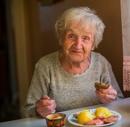 Seniorin sitzt am Küchentisch und isst zu Mittag