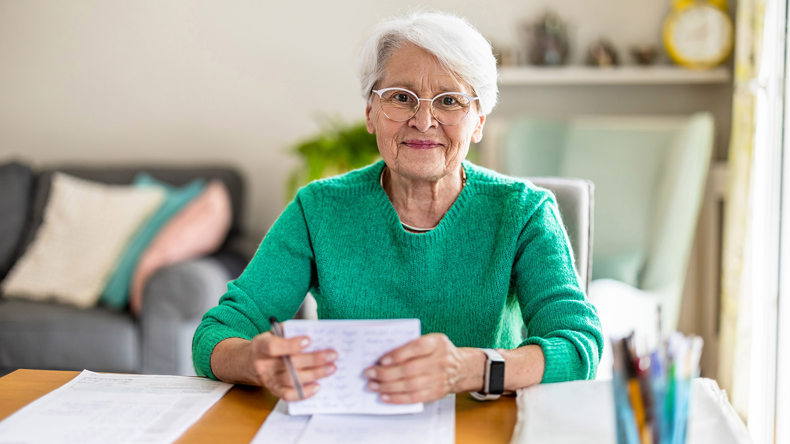 Seniorin erledigt am Schreibtisch Papierarbeit und legt einen Notfallordner an.