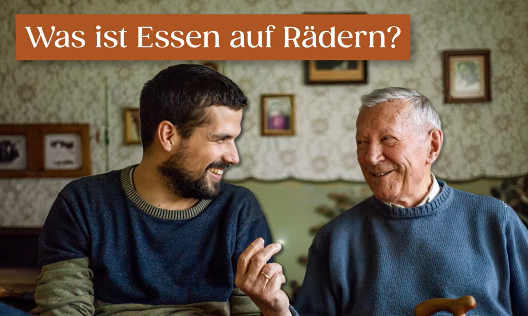 Älterer und jüngerer Mann sitzen am Tisch und unterhalten sich